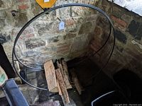 Photo taken from above showing circular wrought iron structure holding firewood logs in a corner against a stone wall.