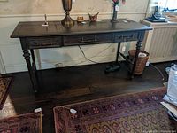 View of the oak library table/desk showing the full table with three drawers, turned legs, and a polished wood surface with some wear.