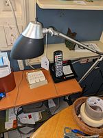 Desk lamp on a wood and metal desk next to a cordless phone and other office items.