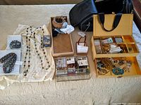 Overall view of assorted jewelry on cloth: necklaces, bracelets, two storage boxes and a black jewelry roll.