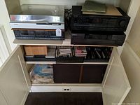 Stereo system components arranged on shelves inside a cabinet showing turntable on top, cassette deck below, receiver and CD player stacked, with CDs, records and speakers stored below.