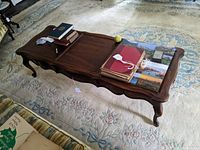Full view of the dark stained wooden coffee table with books and items on top showing overall style and condition.