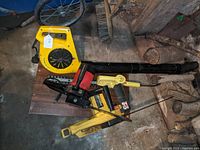 Full view of the yellow leaf blower, yellow hedge trimmer, and the two chainsaws on a wooden surface.