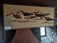 Full view of the framed needlepoint showing a group of five oystercatcher birds with brown, white, black, and orange threads on a beige fabric background.
