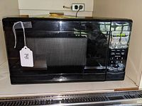 Front view of the black Insignia microwave oven on countertop with digital keypad and clock display showing 11:54