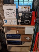 Multiple original retail boxes containing various stemware sets stacked on a shelving unit.
