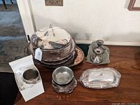 Photo showing all items on a table including the large round covered dish, pair of weighted candlesticks, bowls, trays, and boxed metal holder.