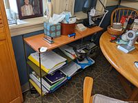Shelf unit from side showing orange top, black metal supports and multiple colored shelves with papers and office items.