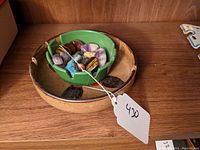 Mixed polished natural stones arranged inside a green ceramic dish which is nested in a larger beige ceramic dish with floral design and notched rim.