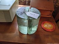 Photo of the pair of aqua colored glass half cylinder bookends placed next to each other on a wooden surface with a white tag labeled 417.