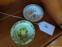 Two small round cloisonné dishes side by side, one with flowers and one with squash design.