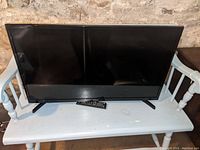 Front view of Samsung 32-inch TV showing screen and stand legs with remote on the bench below the TV.