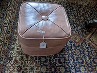 Top angled view of pink square ottoman with button-tufted top and stitched detailing, showing overall good condition.