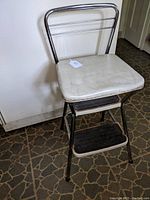 Photo of front and side view of vintage Cosco step stool showing padded white vinyl seat, chrome frame, two black rubber steps, and chrome backrest.