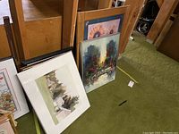 Six artworks leaning against wooden shelving on green carpet