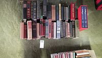 Overview photo showing approximately 30 hardcover books aligned, showcasing various sizes and bindings in worn condition.
