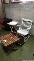Photo of vintage wooden rocking chair, wooden folding TV tray, wooden collapsible patio table, and a magazine rack in basement setting on green carpet