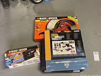 Fixit cordless drill set boxed with Black & Decker hand saw and finishing sander boxed on gray floor