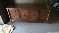 Front view of closed mid century modern wood entertainment cabinet with decorative front panels and legs.