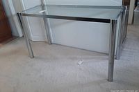 Glass side table with clear glass top, chrome legs, and frame on light carpet