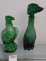 Front view of green glass eagle and dog shaped decanters side by side