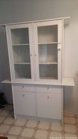 Full view of white kitchen hutch with glass upper doors and solid lower cabinets with drawers, showing general condition and design