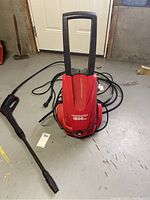 Full view of red Powerwasher pressure washer with hose and spray gun attachment on the floor.