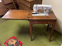 Sewing machine extended with side panels unfolded in wooden cabinet, showing the workspace and machine controls.