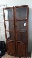 Front view of tall wood and glass display cabinet with two glass paneled upper doors and two lower wooden doors.
