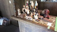 Multiple wood figures and carvings arranged on a wooden surface including human, animal figures, a music box and candles.