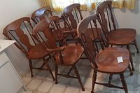 Six solid wood maple dining chairs grouped together showing arm and side chairs with medium brown finish.