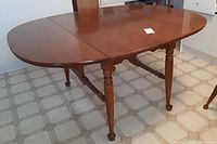 Mid-century solid wood maple dining table with two extension leaves installed, showing entire table with turned legs and wood grain surface