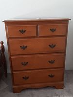 Front view of mid-century solid wood maple dresser showing five drawers and metal handles, with minor surface scratches.