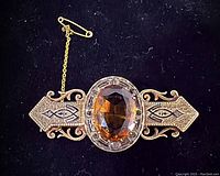 Front view of brooch showing oval citrine center and engraved filigree ends on black background