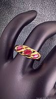 Front angle of the 10kt yellow gold ring with three red ruby stones on a black display hand, showing twisted design and stone setting.