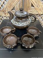 Overall view of porcelain teapot and four matching tea cups set on black surface with woven natural backdrop