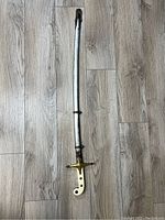 Full view of the antique sword in its sheath on a wood laminate floor