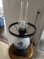 Photo of antique table lamp highlighting glass globe base with blue floral designs and ornate metal base, cord visible.