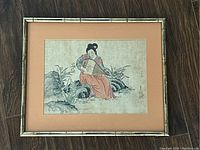 Full view of framed Asian hand-painted artwork of a lady playing a musical instrument seated on rocks.