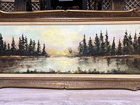 Full view of the vintage oil painting showing landscape with trees and water under a golden sky in an ornate wooden frame.