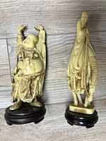 Pair of Asian Buddha statues on wooden bases, shown together on a wood floor background.