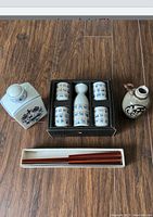 Overview of assorted wine and sake items including boxed sake set, ceramic decanter, vase, and chopsticks on wooden floor