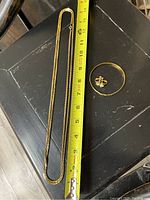 Gold tone necklace about 16 inches long, a gold tone bracelet, and a pair of stud earrings on a dark surface with measuring tape beside necklace