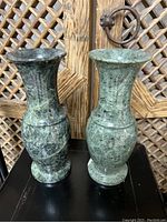 Pair of green vintage marble vases standing side by side on a black surface with wooden background