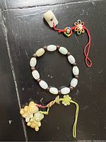 Photo showing jade beaded bracelet with multicolored beads and carved jade pendants with braided cords on a black background
