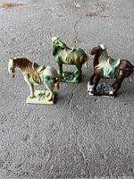 Three vintage tri-color glazed ceramic horse figurines displayed on grey stone surface, showing detail and color of each horse.