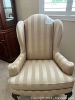 Full view of beige and gold vertically striped wingback chair.