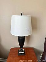 Full view of the black metal and lucite lamp with white shade on a wooden table.