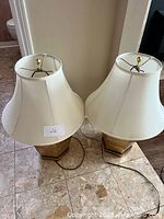 Pair of two ginger jar shaped brass lamps with offwhite bell shades on a stone tile floor.