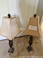Pair of dark metal table lamps with square beige shades, placed side-by-side showing their design and shading details.